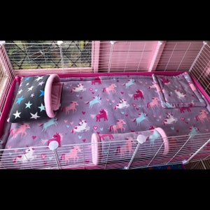 May include: A small animal cage bedding set featuring a purple fleece liner with a repeating pattern of pink, white, and blue unicorns and hearts. The set includes a matching bolster pillow, a square pad, and a black pillow with blue stars.