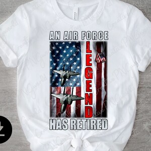 May include: White t-shirt featuring a red, white and blue American flag design. The text "An Air Force Legend Has Retired" is printed on the shirt. Two fighter jets are flying over the flag.
