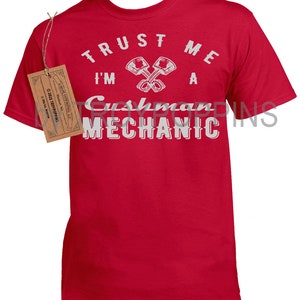 May include: Red t-shirt with white text that reads "Trust me I'm a Cushman Mechanic" with a graphic of two crossed wrenches.
