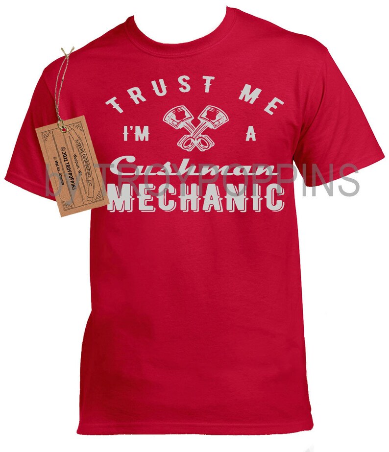 May include: Red t-shirt with white text that reads "Trust me I'm a Cushman Mechanic" with a graphic of two crossed wrenches.