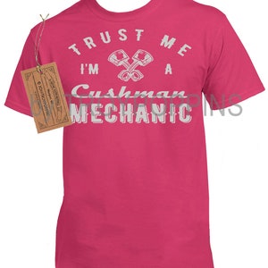 May include: Pink t-shirt with a white graphic that says "Trust me I'm a Cushman Mechanic" with a crossed wrench design.