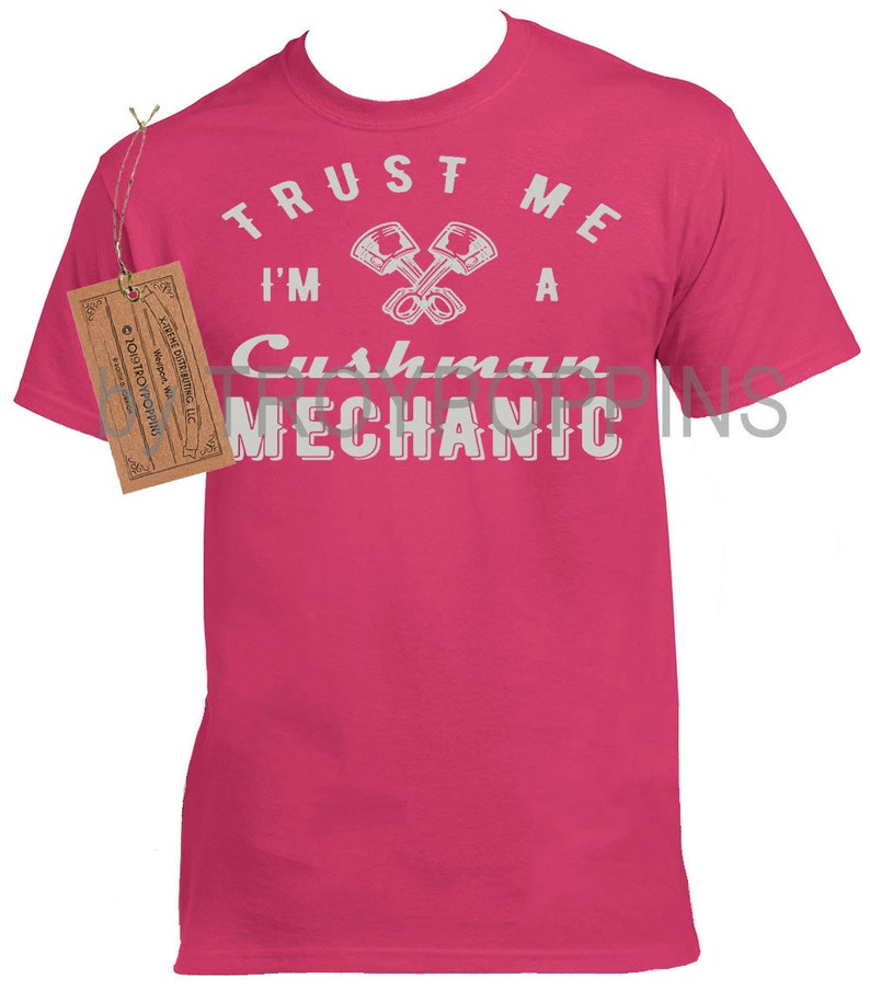 May include: Pink t-shirt with a white graphic that says "Trust me I'm a Cushman Mechanic" with a crossed wrench design.