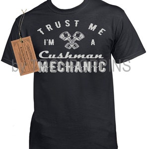 May include: A black t-shirt with a white graphic that says "Trust me I'm a Cushman Mechanic" with a pair of crossed pistons.