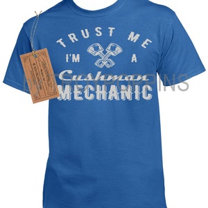 May include: A royal blue t-shirt with white text that reads "TRUST ME I'M A CUSHMAN MECHANIC". The text is in a circle with two crossed wrenches in the center.