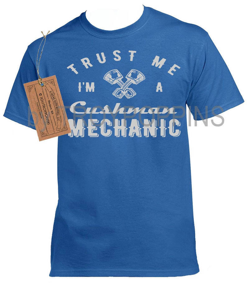 May include: A royal blue t-shirt with white text that reads "TRUST ME I'M A CUSHMAN MECHANIC". The text is in a circle with two crossed wrenches in the center.