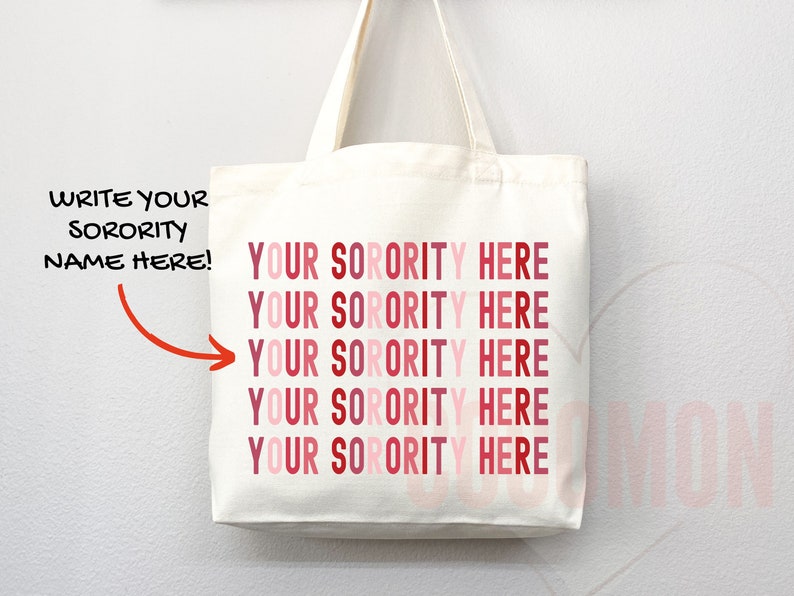 Op de afbeelding: Witte canvas draagtas met de tekst "YOUR SORORITY HERE" die vijf keer wordt herhaald in roze en rode tinten. De tekst "WRITE YOUR SORORITY NAME HERE!" staat in het zwart aan de linkerkant van de tas.