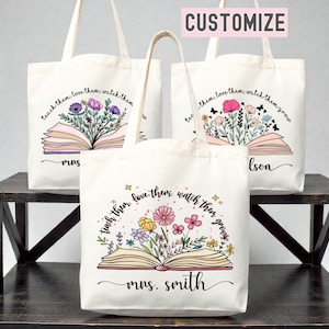 Pu&ograve; includere: Borse tote in tela color crema con disegni floreali e la scritta "teach them, love them, watch them grow". Le borse presentano un libro aperto con fiori colorati. Una borsa &egrave; personalizzata con "mrs. smith."