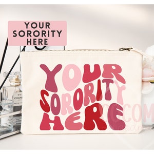 May include: A white canvas makeup bag with a zipper closure. The bag features a pink and red graphic design with the text "YOUR SORORITY HERE" in a retro font.