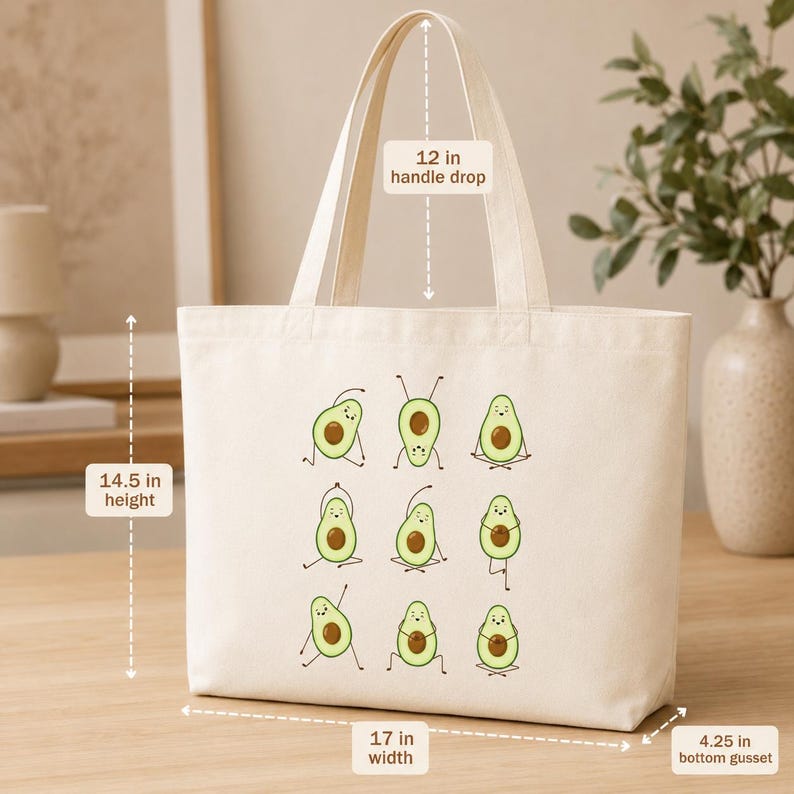 May include: Cream-colored tote bag with a 12-inch handle drop, 14.5-inch height, 17-inch width, and 4.25-inch bottom gusset. The bag features a print of cartoon avocados in yoga poses. The bag is made of a sturdy fabric.