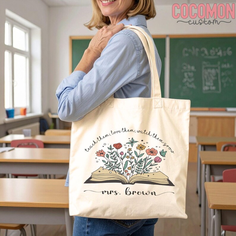 Pu&ograve; includere: Borsa tote color crema con un libro aperto da cui sbocciano fiori colorati. Il testo recita "teach them, love them, watch them grow" e "mrs. Brown". La borsa &egrave; tenuta da una persona in un'aula, con una lavagna sullo sfondo.