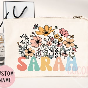 May include: A white canvas makeup bag with a floral design and the name "SARAH" in colorful, retro-style lettering.