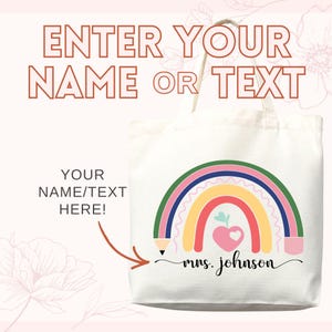 May include: A white canvas tote bag with a colorful rainbow design. The rainbow includes red, yellow, green, and blue arches, with a pink heart and apple. Text on the bag reads "ENTER YOUR NAME OR TEXT" and "YOUR NAME/TEXT HERE!"