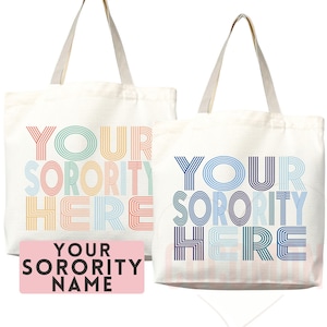 May include: Two white canvas tote bags with colorful striped text that reads "Your Sorority Here". One bag has rainbow stripes and the other has blue stripes. A pink rectangle with black text reads "Your Sorority Name".