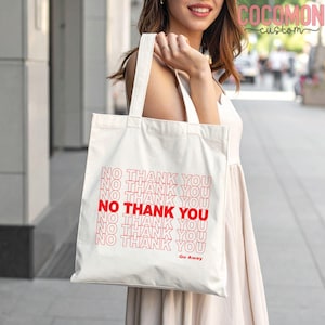 May include: A white canvas tote bag with red text that reads "NO THANK YOU" repeated multiple times. The words "Go Away" are printed at the bottom. The bag has two handles and is being held by a person.