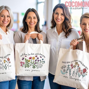 May include: Four women holding white tote bags with floral designs and the text "teach them, love them, watch them grow." Each bag features a different floral arrangement and a name. The bags have beige handles.
