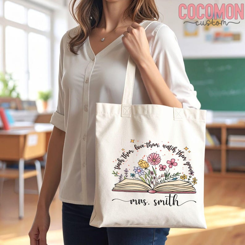 Pu&ograve; includere: Borsa tote color crema con design floreale e libro aperto. Il testo recita "teach them, love them, watch them grow" e "mrs. smith". La borsa ha manici lunghi.