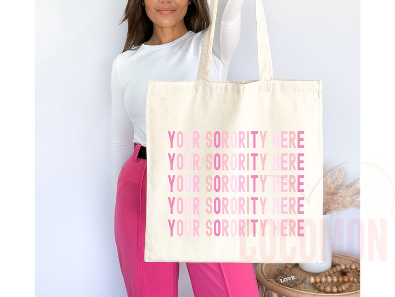 Op de afbeelding: Een witte canvas tote bag met de tekst "YOUR SORORITY HERE" vijf keer herhaald in roze letters, met een verloop van lichtroze naar donkerroze.