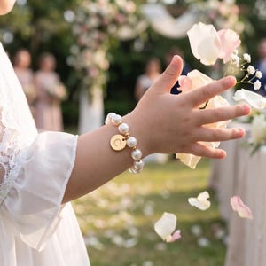 A person's hand holding a bouquet of white and pink flowers, with petals falling around them, in a garden setting with other people in the background.