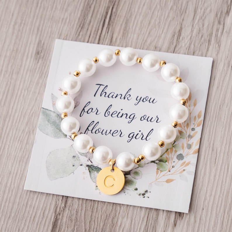 a white bracelet with a gold disc and a thank you for being our flower girl
