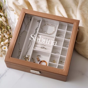 A brown jewelry box with compartments for storing various pieces of jewelry, including rings, necklaces, and bracelets. The word "Sabrina" is written on the front of the box.