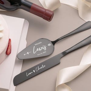 A white cake with a strawberry on top, a wine bottle, and a knife with a personalized message on it, all placed on a white surface.