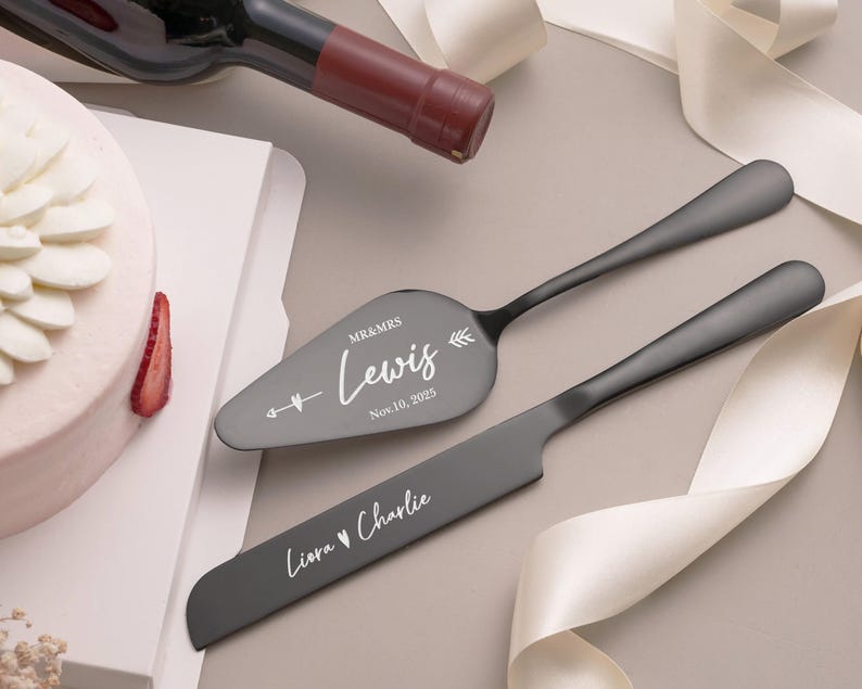 A white cake with a strawberry on top, a wine bottle, and a knife with a personalized message on it, all placed on a white surface.