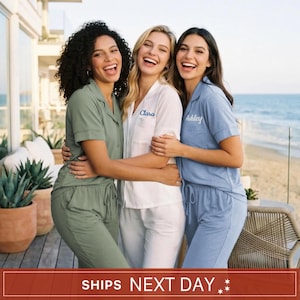 May include: Three sets of button-down pajama shirts and matching pants in sage green, white, and light blue. The white shirt features the name Clara embroidered in blue, and the light blue shirt features the name Ashley embroidered in white.