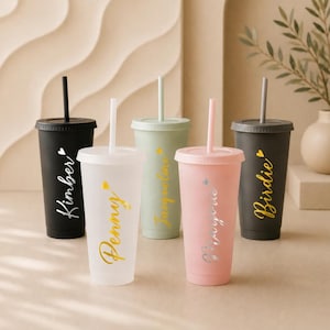 Può includere: Cinque bicchieri personalizzati in vari colori: nero, trasparente, verde salvia, rosa e grigio scuro. Ogni bicchiere ha un coperchio e una cannuccia, con nomi in corsivo dorato o argentato. I nomi includono Kimber, Penny, Jacqueline, Marjorie e Birdie.