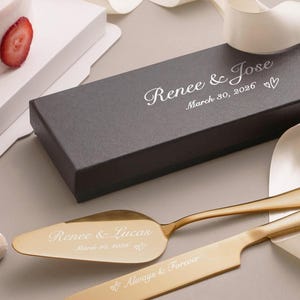 May include: A gold-colored cake server and knife set with the inscription "Renee & Lucas March 30, 2026" on the server and "Always & Forever" on the knife. A dark gray box is visible with the inscription "Renee & Jose March 30, 2026".