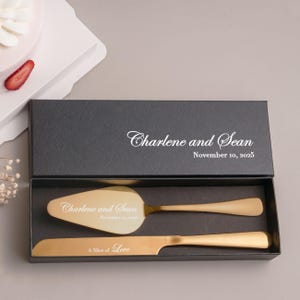 May include: A gold-colored cake server and knife set inside a black gift box. The server and knife are engraved with the names "Charlene and Sean" and the date "November 10, 2025". The knife is engraved with the phrase "A Slice of Love".
