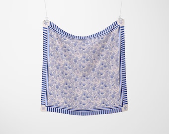 Peut inclure: Un foulard carré arborant un motif répétitif de coquillages, d'étoiles de mer et de dollars des sables bleus sur fond clair. Le foulard est encadré par une bordure rayée bleue et blanche avec de petites icônes de coquillages aux coins.