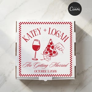 Op de afbeelding: Een witte vierkante pizzadoos met een rood geblokte rand. Op het deksel staat de rode tekst KATEY + LOGAN Are Getting Married OCTOBER 3, 2026, naast een rode lijntekening van een wijnglas en een hand die een puntje pepperoni pizza vasthoudt.