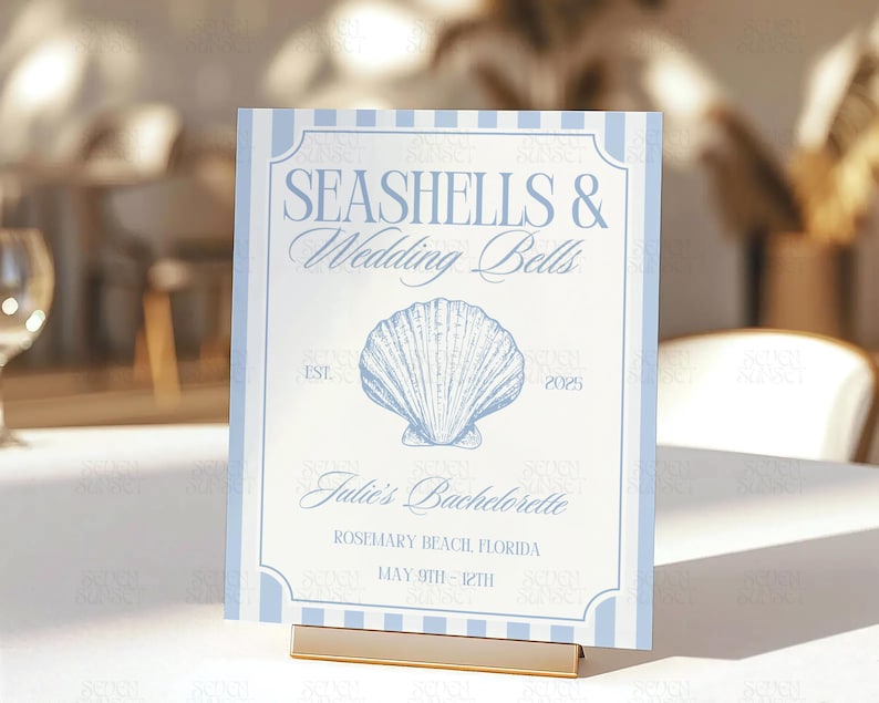 Op de afbeelding: Een lichtblauw en wit bord met de tekst "Seashells & Wedding Bells" en een schelpillustratie. Het bord bevat ook de tekst "Julie's Bachelorette", "Rosemary Beach Florida" en "May 9th - 12th".