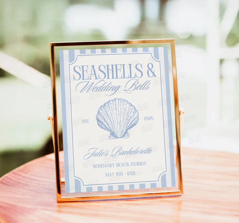 Op de afbeelding: Een lichtblauw en wit gestreept bord met de tekst "Seashells & Wedding Bells" in een decoratief lettertype. Het bord bevat ook een schelpillustratie, de tekst "Julie's Bachelorette", "Rosemary Beach Florida" en "May 9th - 12th".