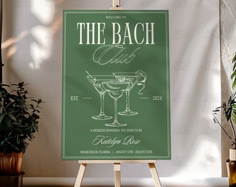 May include: Green welcome sign with white text that reads "Welcome to The Bach Club Est. 2024" with a drawing of three martini glasses. The sign also says "A weekend honoring the bride to be Katelyn Rose Miami Beach, Florida August 12th - August 15th"