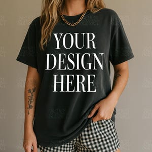 May include: Black t-shirt with the text "YOUR DESIGN HERE" in white, paired with black and white checkered shorts. A gold chain necklace is worn. The shirt is a dark color, and the shorts have a classic pattern.
