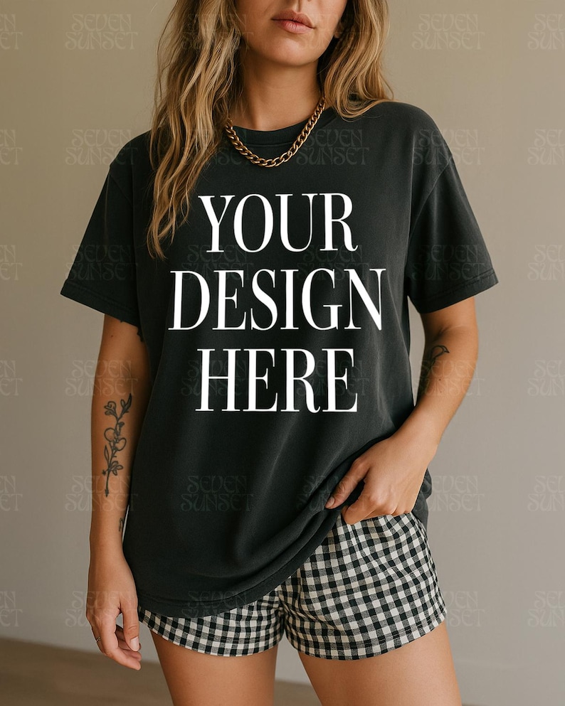 May include: Black t-shirt with the text "YOUR DESIGN HERE" in white, paired with black and white checkered shorts. A gold chain necklace is worn. The shirt is a dark color, and the shorts have a classic pattern.