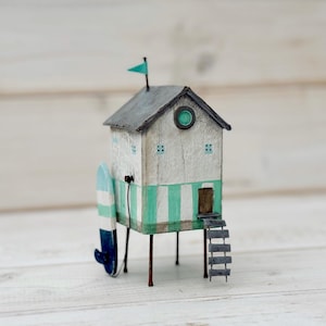 Wolnostojący domek plażowy z drewna dryfującego na palach, z deską surfingową.