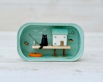 Andato a pesca. Casetta per gatti. Scena in legno galleggiante fatta a mano in una scatola di sardine.