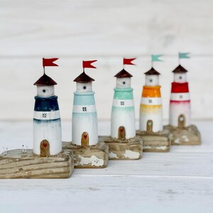 Pu&ograve; includere: Una fila di cinque fari in miniatura in legno. Ogni faro ha una diversa combinazione di colori: blu, azzurro, verde, arancione e rosso. Hanno tetti marroni e piccole bandiere. I fari poggiano su basi rettangolari usurate.