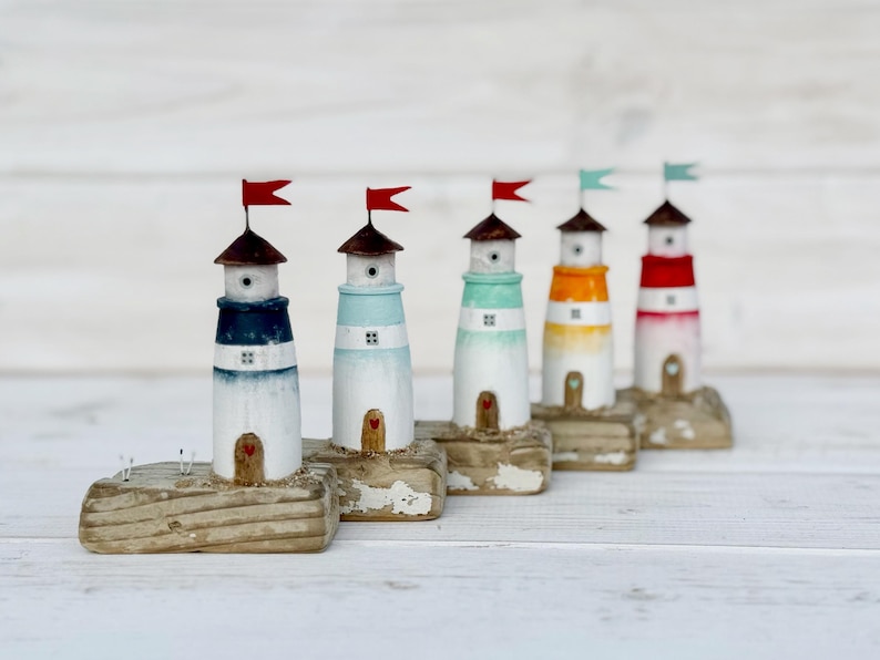 Pu&ograve; includere: Una fila di cinque fari in miniatura in legno. Ogni faro ha una diversa combinazione di colori: blu, azzurro, verde, arancione e rosso. Hanno tetti marroni e piccole bandiere. I fari poggiano su basi rettangolari usurate.