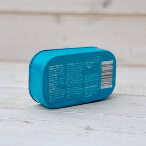 May include: A blue can of sardines in tomato sauce. The can has a label with the text 'Sardines in Tomato Sauce', 'Ingredients', 'Allergy Advice', 'Best Before', 'Storage', 'Caution', 'Nutrition', and '120g e'.
