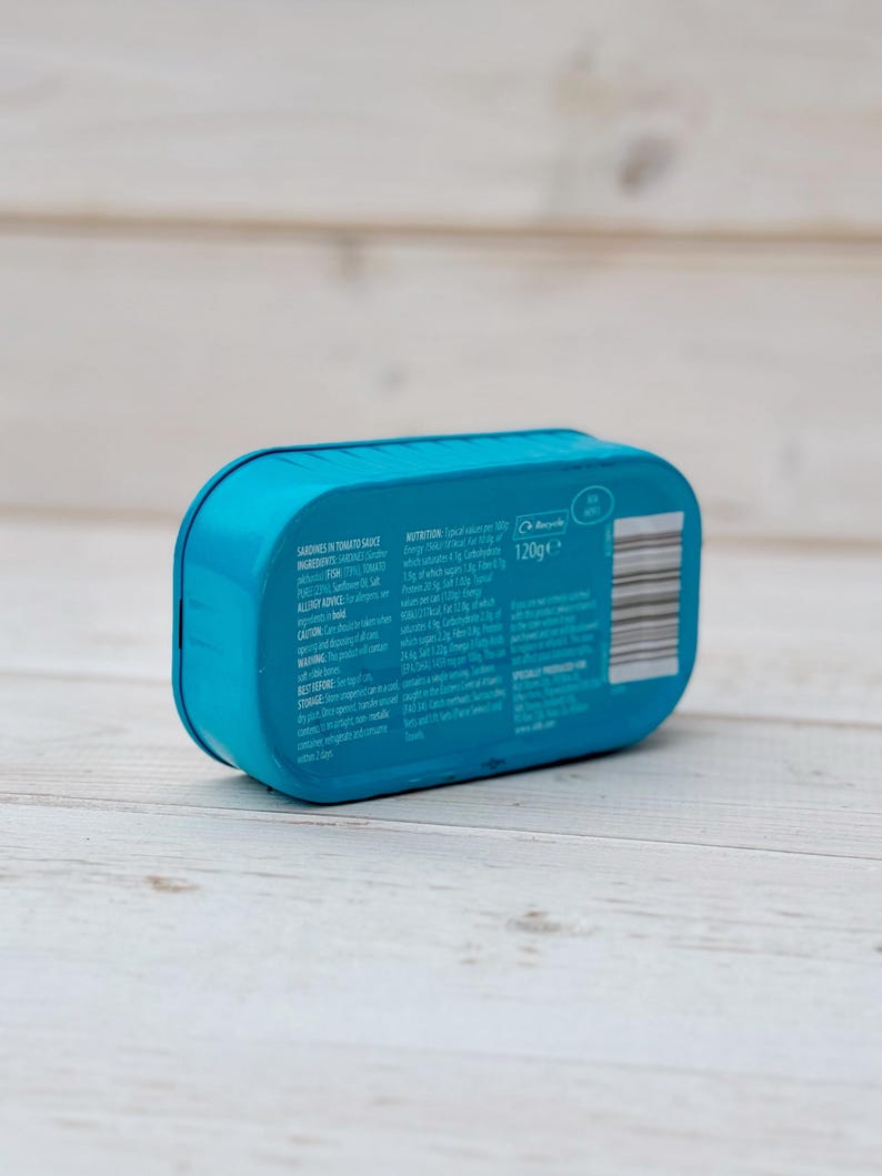 May include: A blue can of sardines in tomato sauce. The can has a label with the text 'Sardines in Tomato Sauce', 'Ingredients', 'Allergy Advice', 'Best Before', 'Storage', 'Caution', 'Nutrition', and '120g e'.