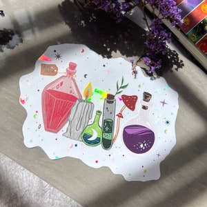 May include: A white sticker with a whimsical design featuring five glass bottles filled with colorful liquids. The bottles are surrounded by stars, moons, and other celestial elements. The sticker also includes a small tag that reads "Ash & Skull".