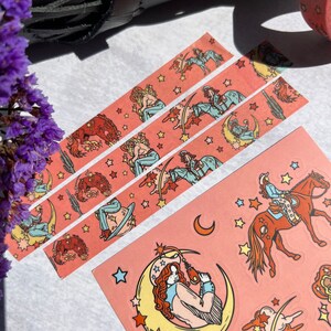 K&ouml;nnte beinhalten: Drei Rollen rosa Washi-Tape mit einem sich wiederholenden Muster einer Frau, die ein Pferd reitet, einem Halbmond und Sternen. Das Klebeband befindet sich auf einer wei&szlig;en Oberfl&auml;che.