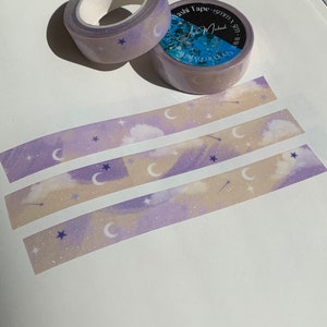 May include: Purple and beige washi tape with a moon and star pattern. The tape is rolled up and has a label that says "Washi Tape 15mm x 10m".