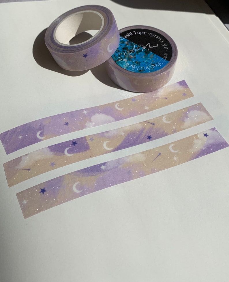 May include: Purple and beige washi tape with a moon and star pattern. The tape is rolled up and has a label that says "Washi Tape 15mm x 10m".