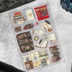 May include: A sheet of clear stickers with illustrations of a bookstore, books, and other book-related items. The stickers include a red storefront with the words "Book Nook" above the door, a stack of books with the words "Read More!" on top, and a bookshelf filled with books. The stickers are perfect for adding a touch of whimsy to journals, planners, and other paper crafts.