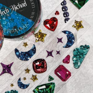 May include: A roll of washi tape with a variety of colorful, glittery, and jewel-toned designs. The designs include hearts, stars, moons, clouds, and diamonds. The tape is 15mm wide and 10m long. The tape is made by Arch Michael.