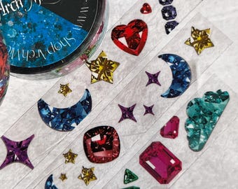 May include: A roll of washi tape with a variety of colorful, glittery, and jewel-toned designs. The designs include hearts, stars, moons, clouds, and diamonds. The tape is 15mm wide and 10m long. The tape is made by Arch Michael.